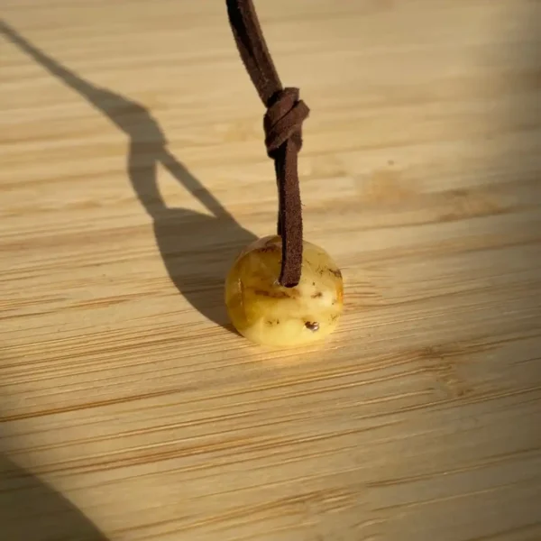 Translucent amber bead pendant on leather cord against a polished wooden surface.