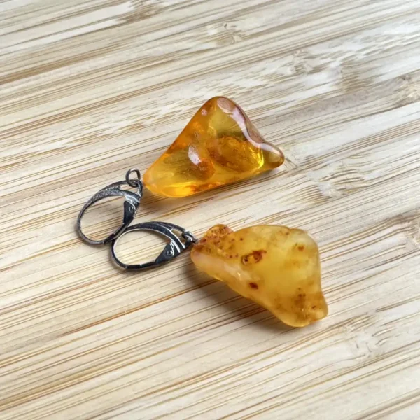 Elegant amber earrings with triangular and rounded shapes on a wooden surface.
