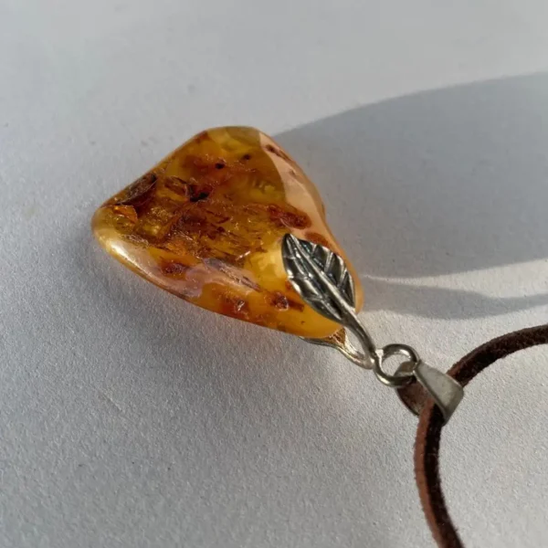 Elegant amber pendant with leaf design, suspended on leather cord for a natural, chic look.