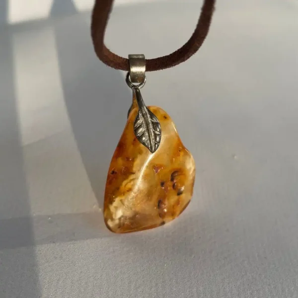 Amber pendant on suede with leaf detail, showcasing natural inclusions and rich hues.