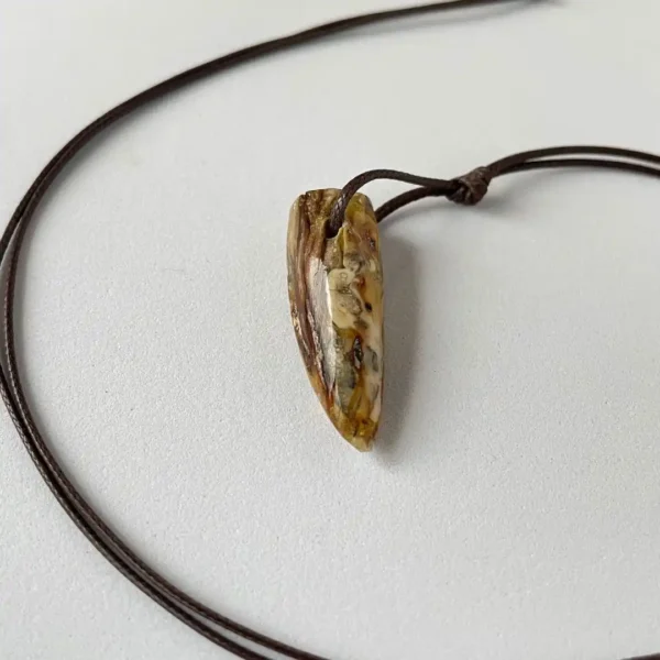 Handcrafted amber pendant on leather cord, featuring natural textures and earthy tones.