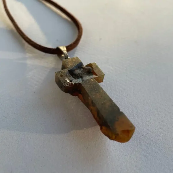 Unique amber cross pendant on brown cord necklace, showcasing artisanal craftsmanship and natural beauty.