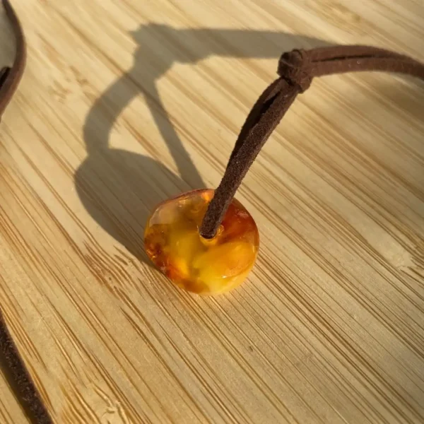 Beautiful amber pendant on leather cord, showcasing natural patterns against a textured wooden background.