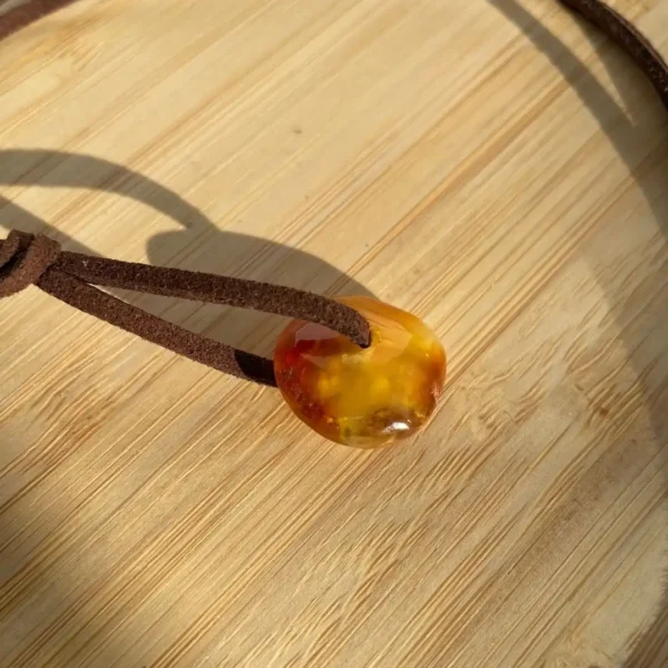 Polished amber pendant on a brown suede cord, showcasing natural inclusions and warm hues.