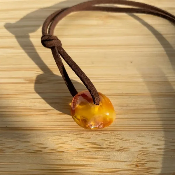 Elegant amber pendant on leather cord, showcasing natural inclusions against a wooden background.