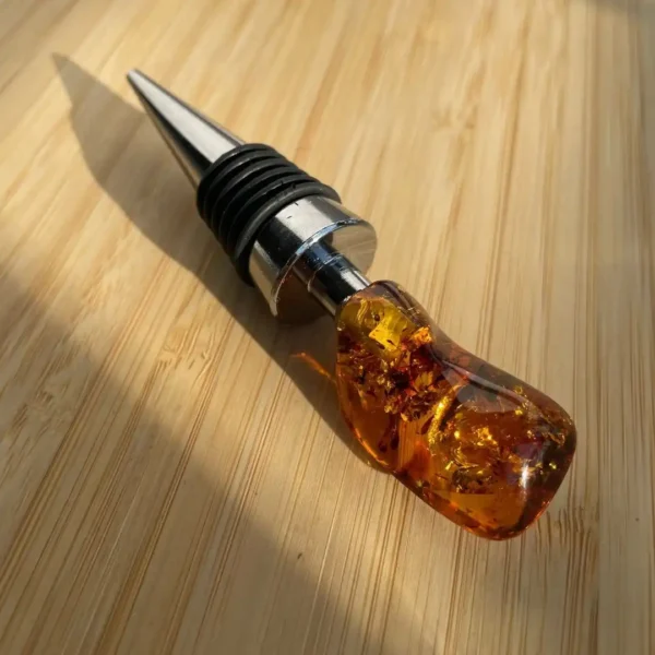 Elegant wine bottle stopper with amber resin handle and sleek metal finish on wooden surface.