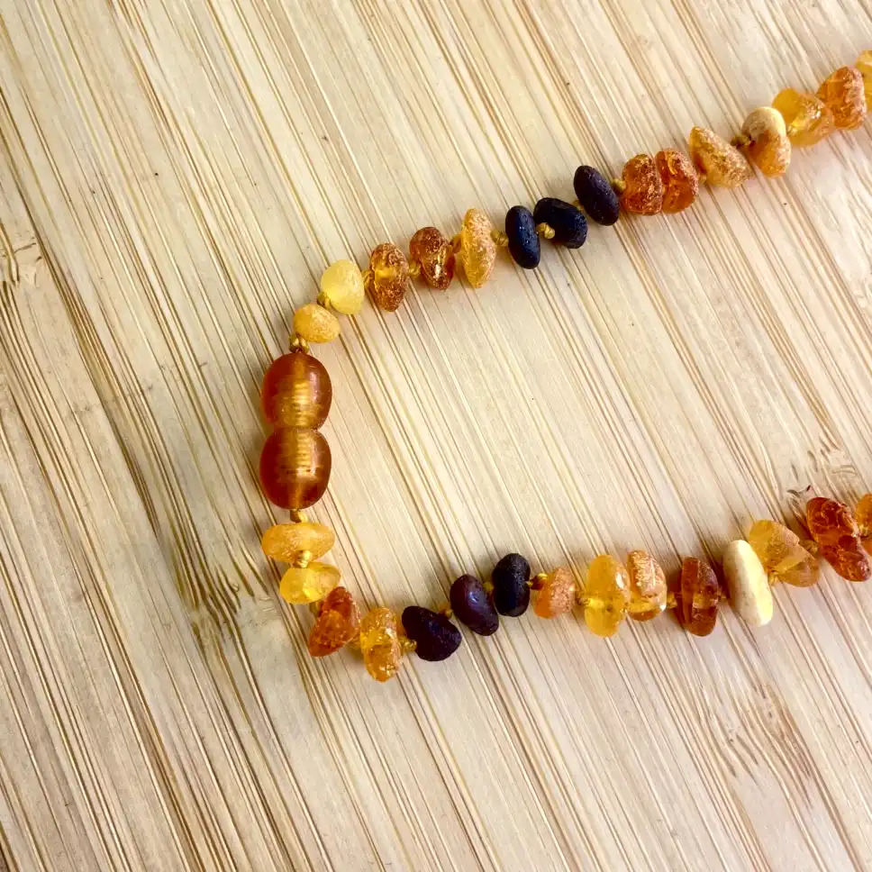 Stunning amber teething necklace showcasing vibrant hues, natural textures, and artisanal craftsmanship on wood backdrop.