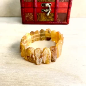 Amber Bracelet with Medium Stones displayed beside a vibrant red chest, showcasing natural stones beauty and craftsmanship.
