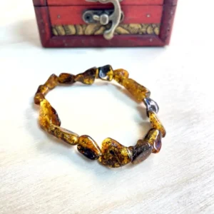 Elegant amber nugget bracelet with rich hues displayed on a light wooden surface and decorative box.