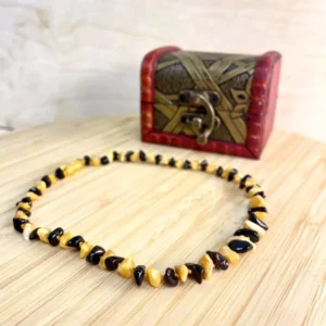 Amber necklace with polished stones displayed beside a vintage-style chest on wood.