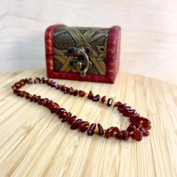 Amber necklace draped elegantly on a wooden surface beside a decorative red chest.