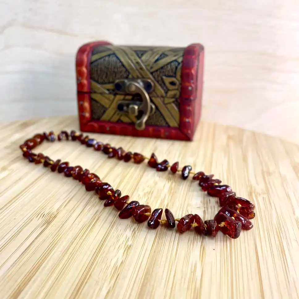 Amber necklace draped elegantly on a wooden surface beside a decorative red chest.