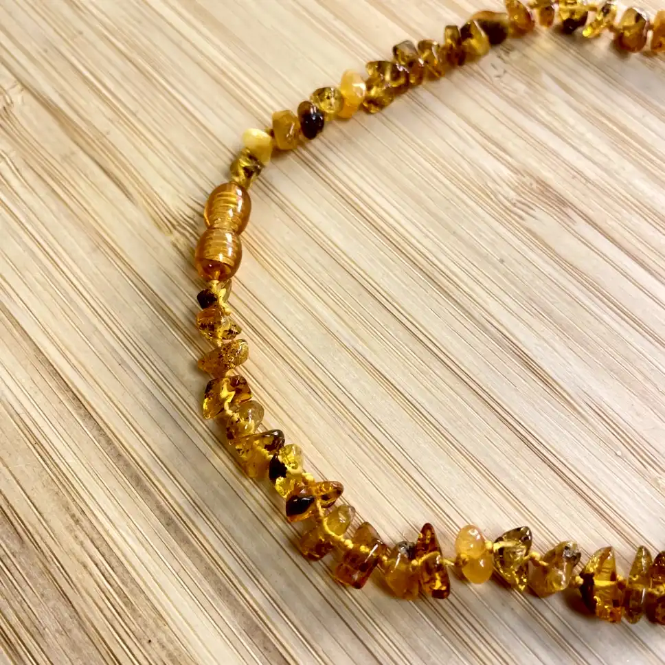 Elegant amber teething necklace featuring unique beads in rich golden hues on a natural wood background.