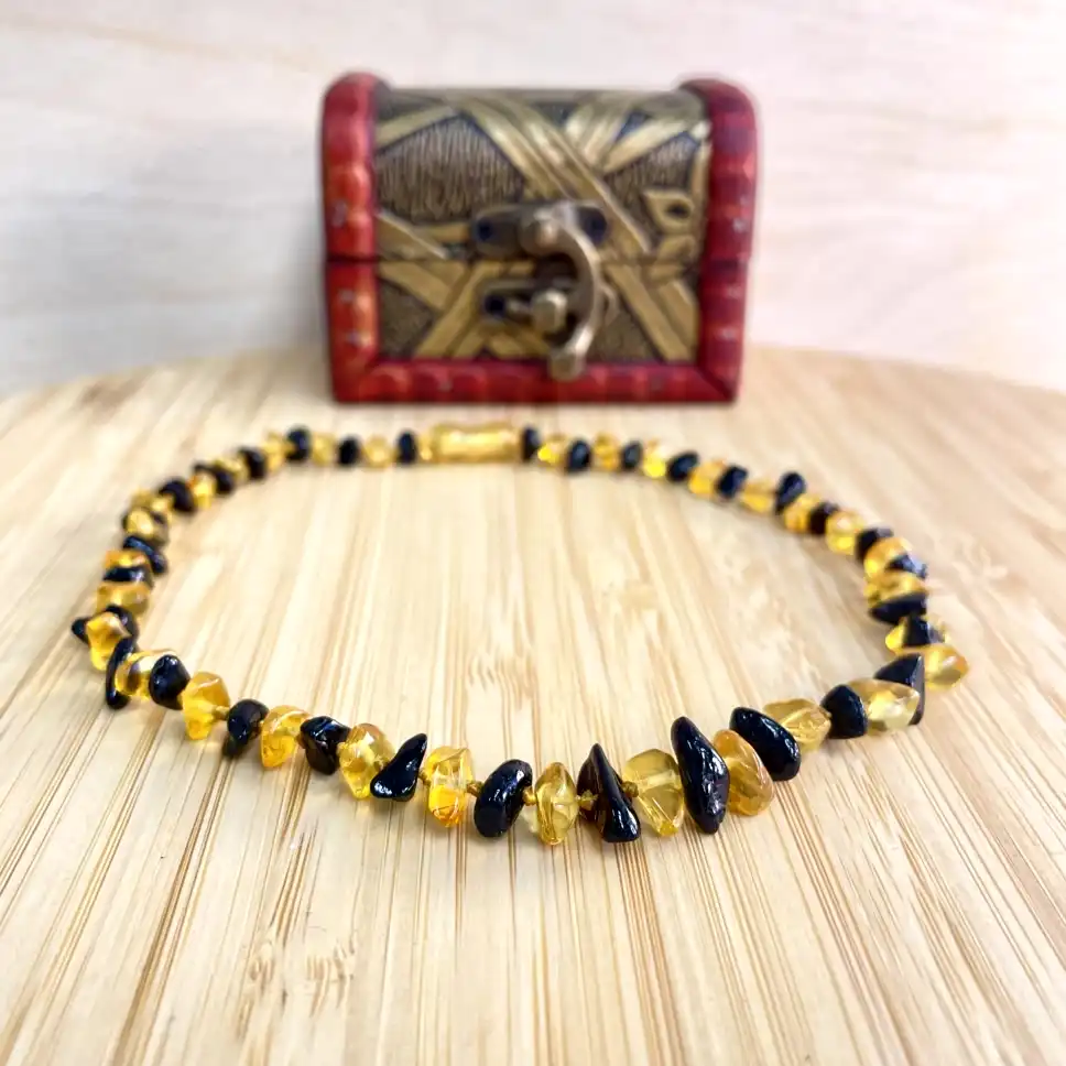 Stunning amber and black bead necklace displayed on wood, accompanied by an elegant decorative box.