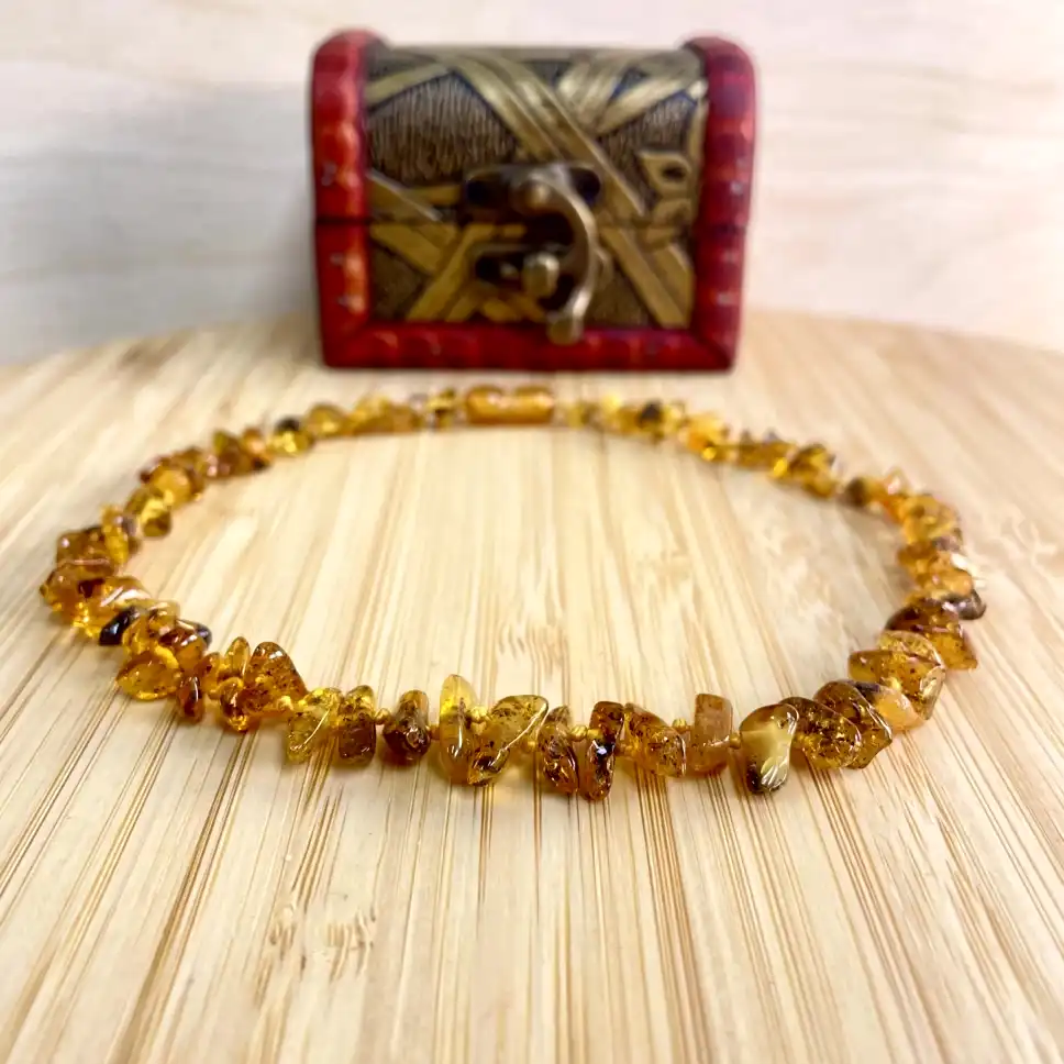Elegant amber teething necklace on wood, showcasing unique beads and a decorative red chest background.