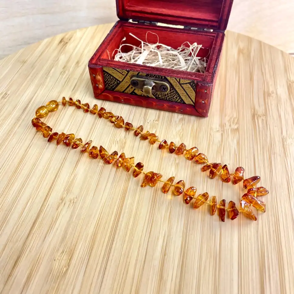 Amber necklace elegantly displayed beside an ornate red wooden box on a bamboo surface.