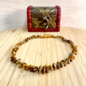 Amber necklace on a wooden surface beside a decorative red chest, showcasing natural beauty.