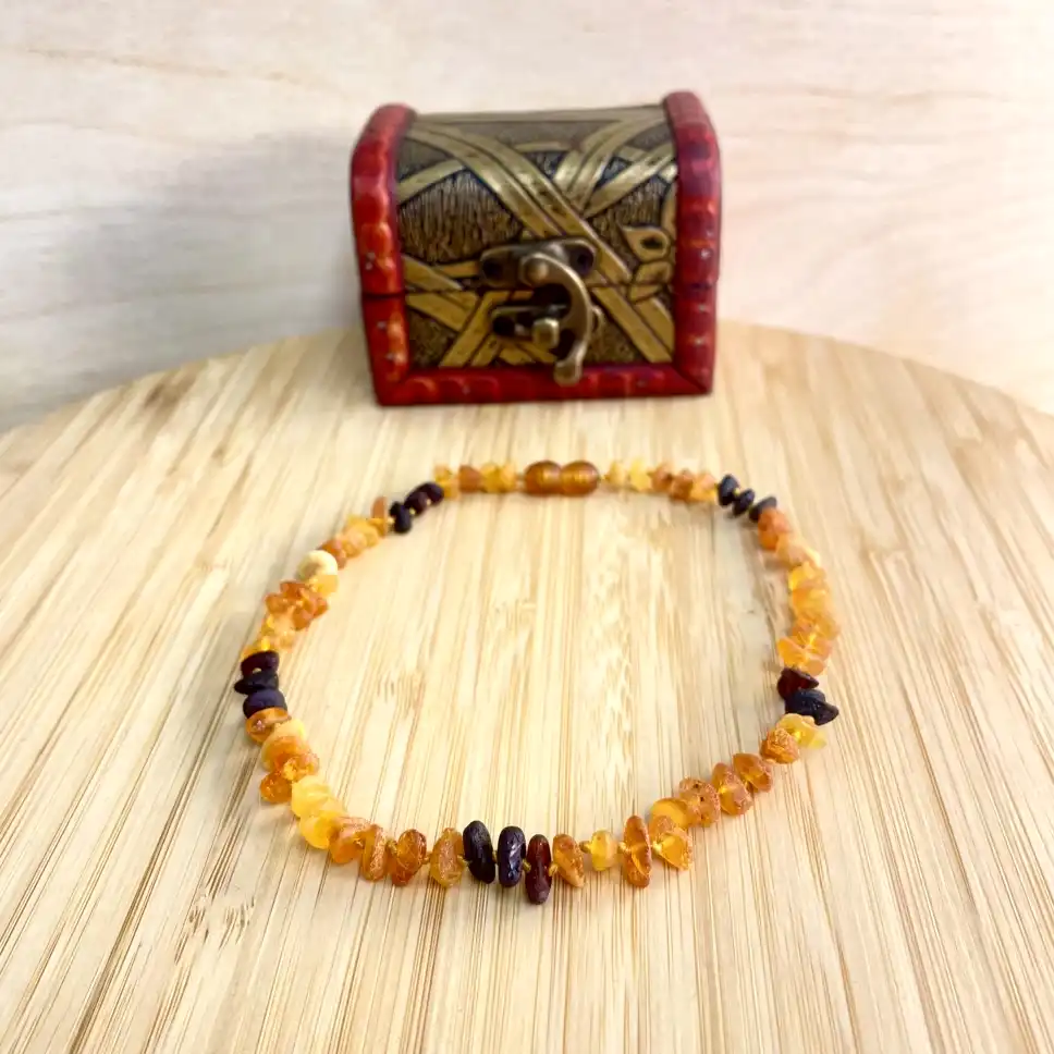 Elegant amber teething necklace displayed on a wooden platform beside an ornate treasure chest.