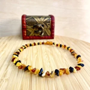 Elegant amber teething necklace displayed on wood, beside a decorative chest, showcasing warm colors and natural beauty.
