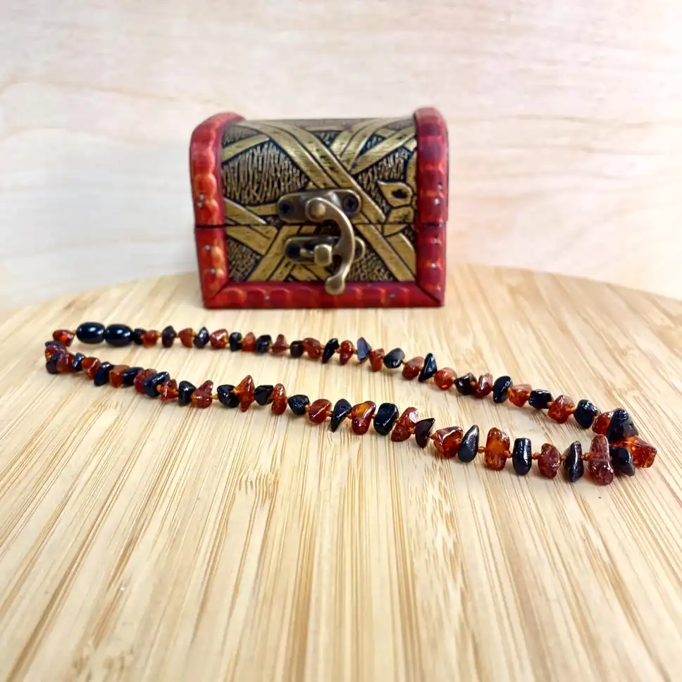 Elegant amber teething necklace resting on a decorative wooden chest, showcasing natural beauty and craftsmanship.