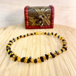 Amber teething necklace with dark beads resting on a vintage wooden chest, showcasing natural elegance.