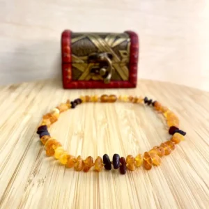 Elegant amber teething necklace displayed on wooden surface, accompanied by a decorative chest.