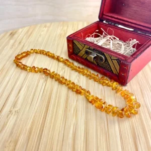 Elegant amber necklace resting on a wooden surface, accompanied by a decorative red treasure box.