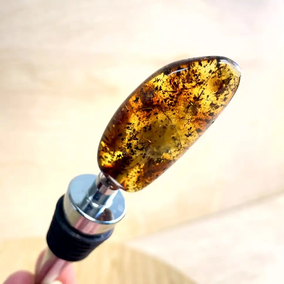 Elegant amber bottle stopper with a polished metal handle, showcasing unique inclusions and natural beauty.