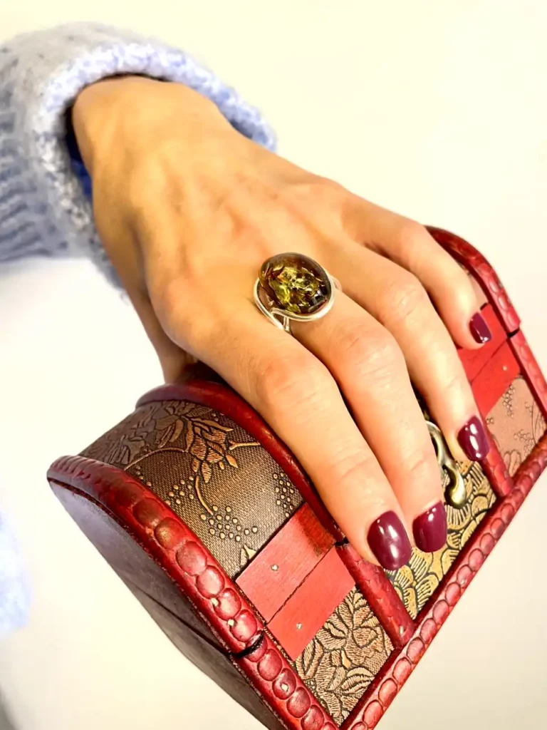 Elegant hand holding ornate red box with amber ring, showcasing refined craftsmanship and style.