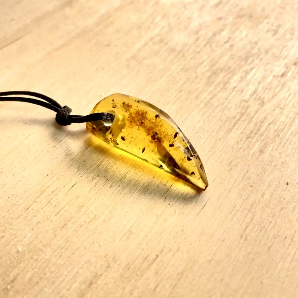 Elegant Amber Pendant Necklace on a natural wooden surface, showcasing its golden hue and unique inclusions.