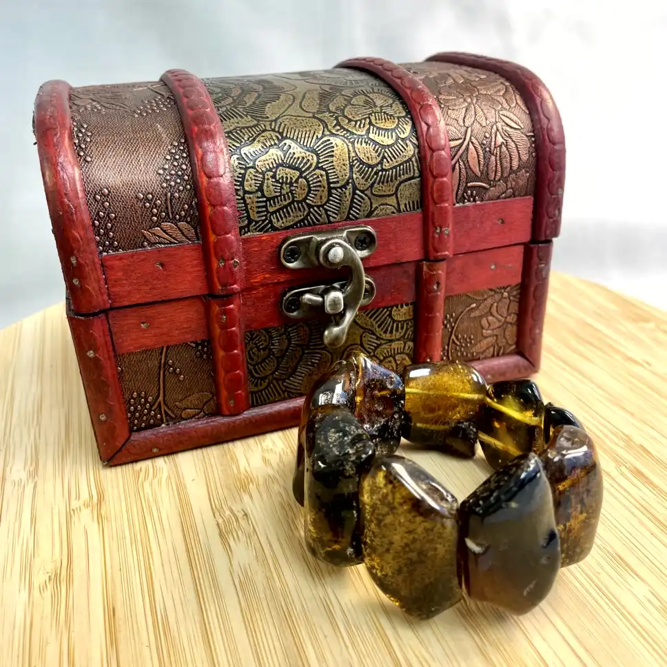Antique treasure chest with ornate patterns and a polished amber bracelet on wooden surface.