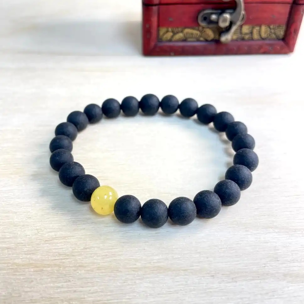 Elegant black and yellow beaded bracelet featuring a striking amber centerpiece in a decorative box.