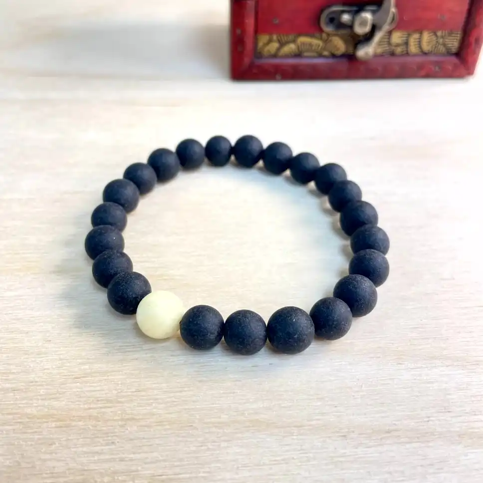 Elegant black amber bead bracelet with cream accent on a warm wooden surface.