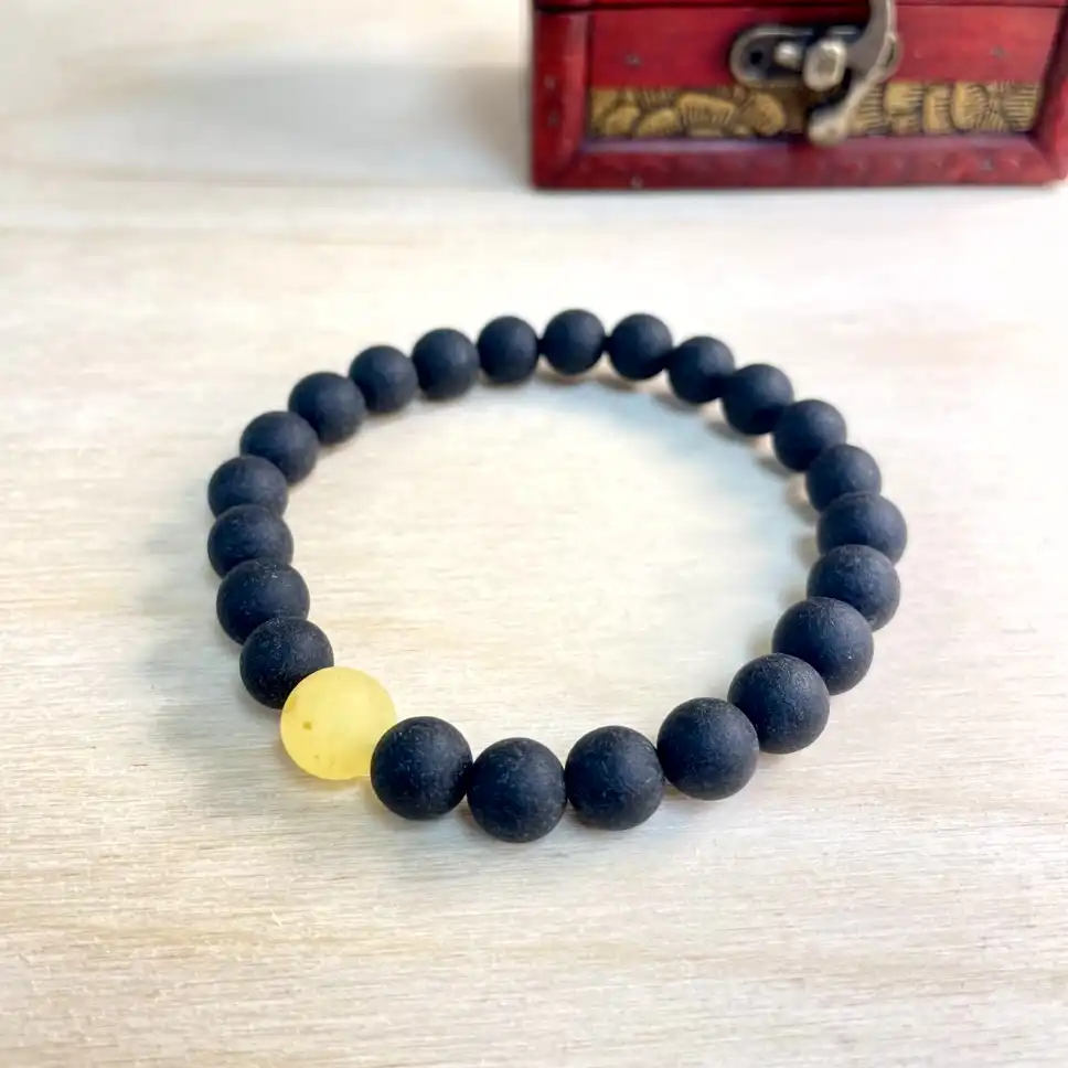 Elegant black bead bracelet with a vibrant amber accent, beautifully displayed with a decorative chest.