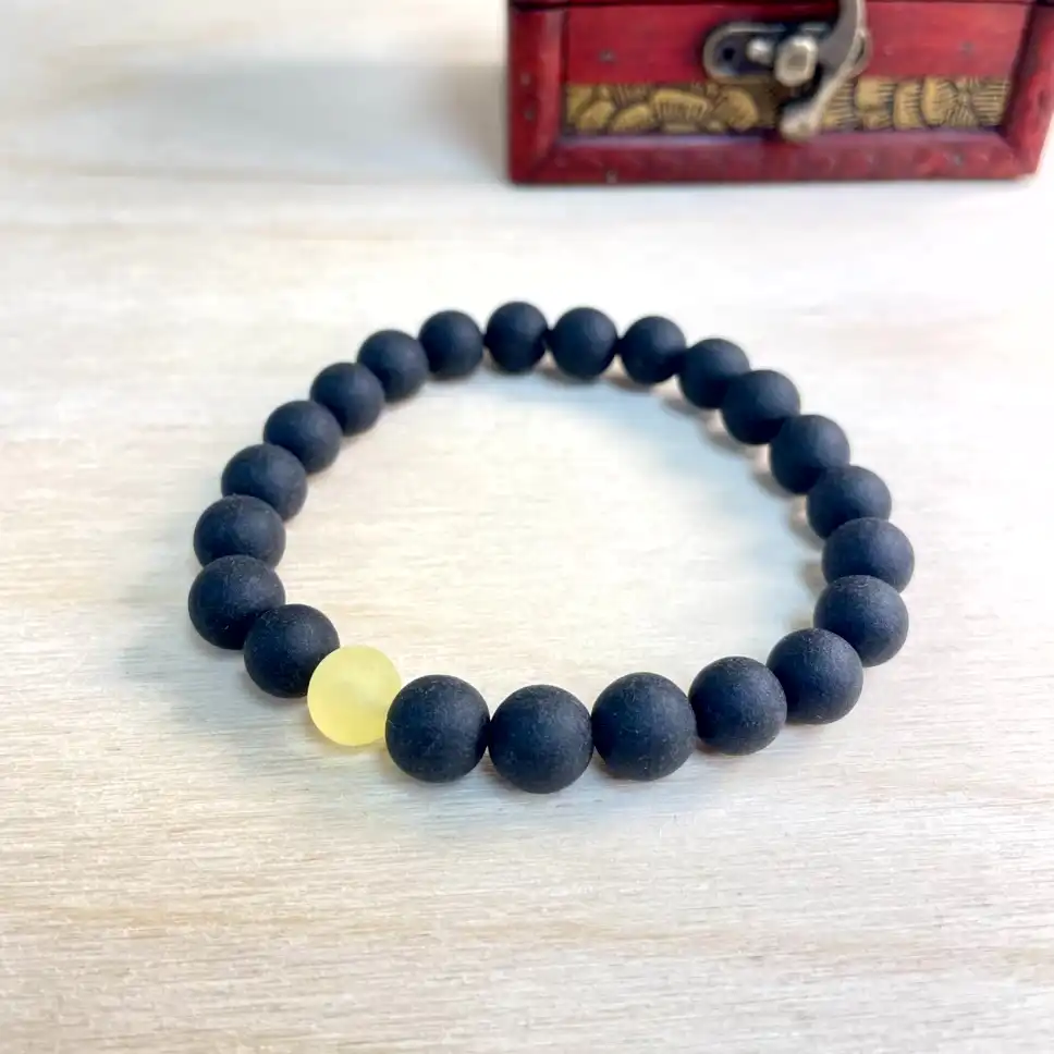Elegant black amber bead bracelet with amber yellow accent on a decorative wooden box.