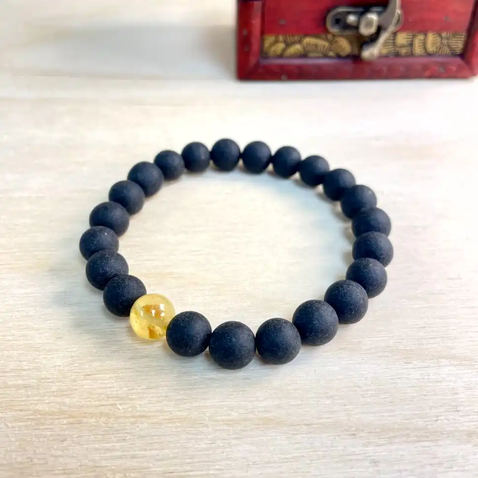 Sleek matte black amber bead bracelet with a striking amber focal bead against a warm wooden backdrop.