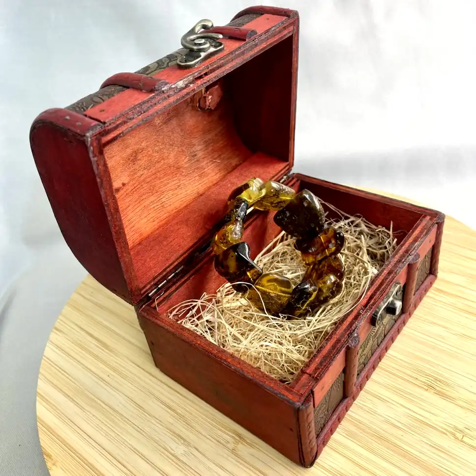 Vintage red box with intricate designs containing a beautiful amber bracelet nestled inside.