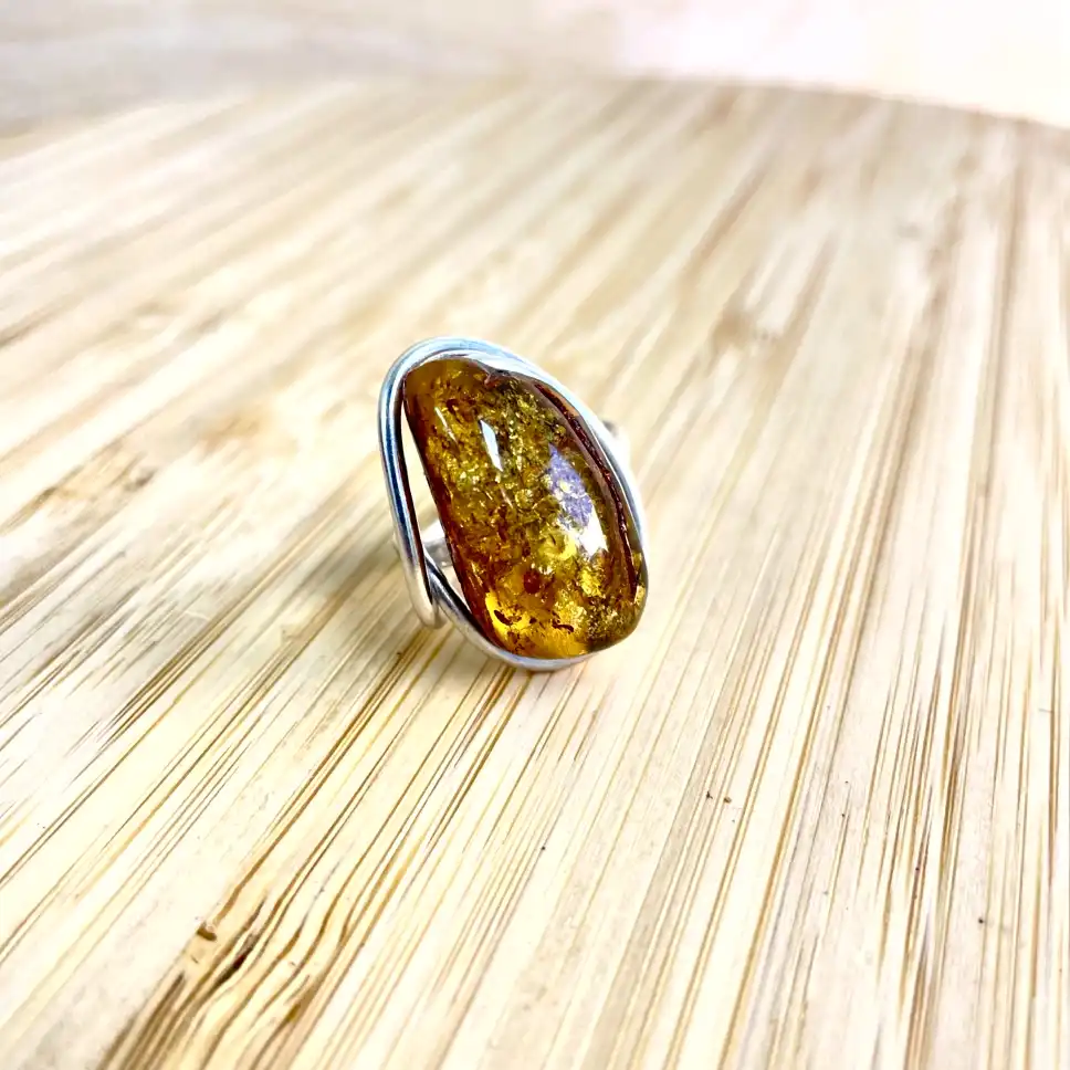 Stunning amber ring with silver plating, showcasing natural inclusions and modern design on wooden surface.