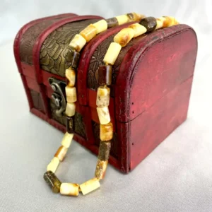 Elegant amber bead necklace atop a vintage red chest, showcasing artisan craftsmanship and natural beauty.