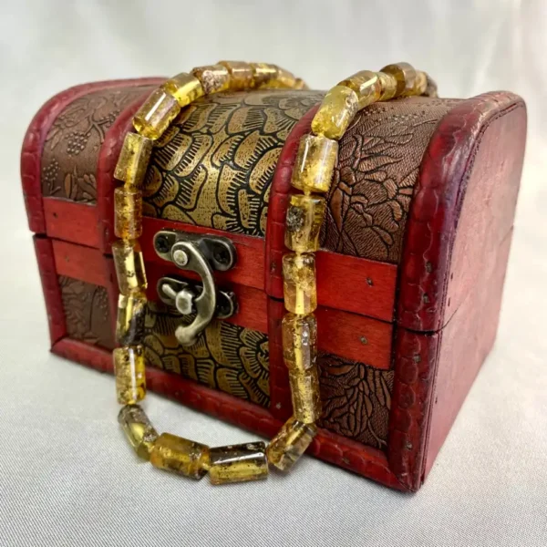 Antique treasure chest with intricate carvings and amber bead necklace on a neutral fabric background.