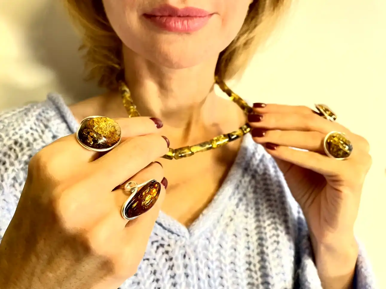 Elegant woman showcasing luxurious amber jewelry, featuring a chunky necklace and stunning rings.