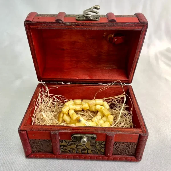 Red wooden treasure chest with elegant bracelet, nestled in straw, showcasing exquisite craftsmanship.