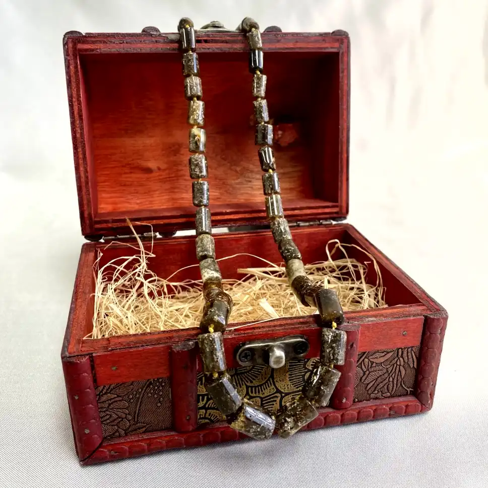 Intricately designed wooden jewelry box opens to reveal a stunning handmade necklace and straw bedding.